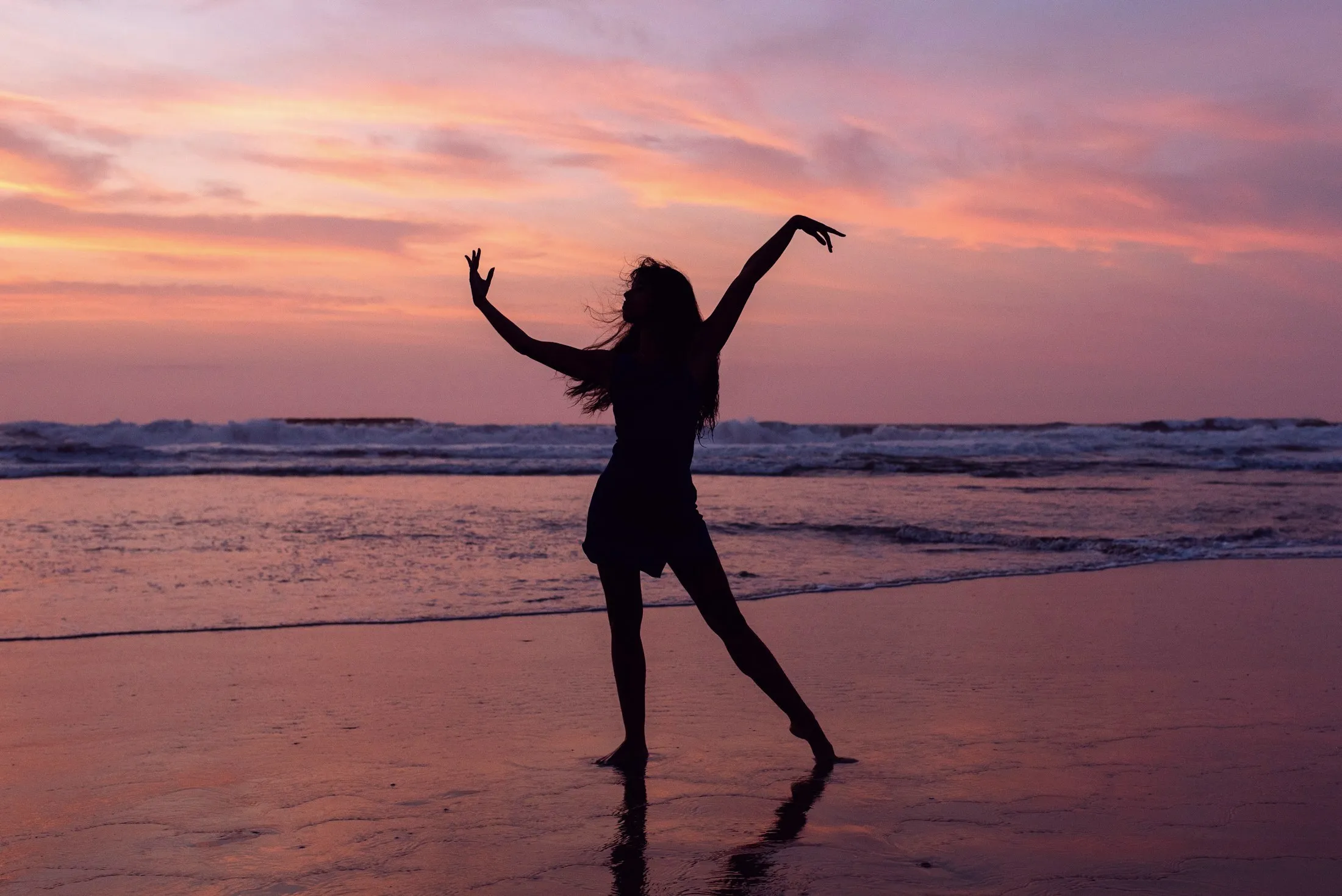 A woman dancing freely on the beach under a lilac sunset sky