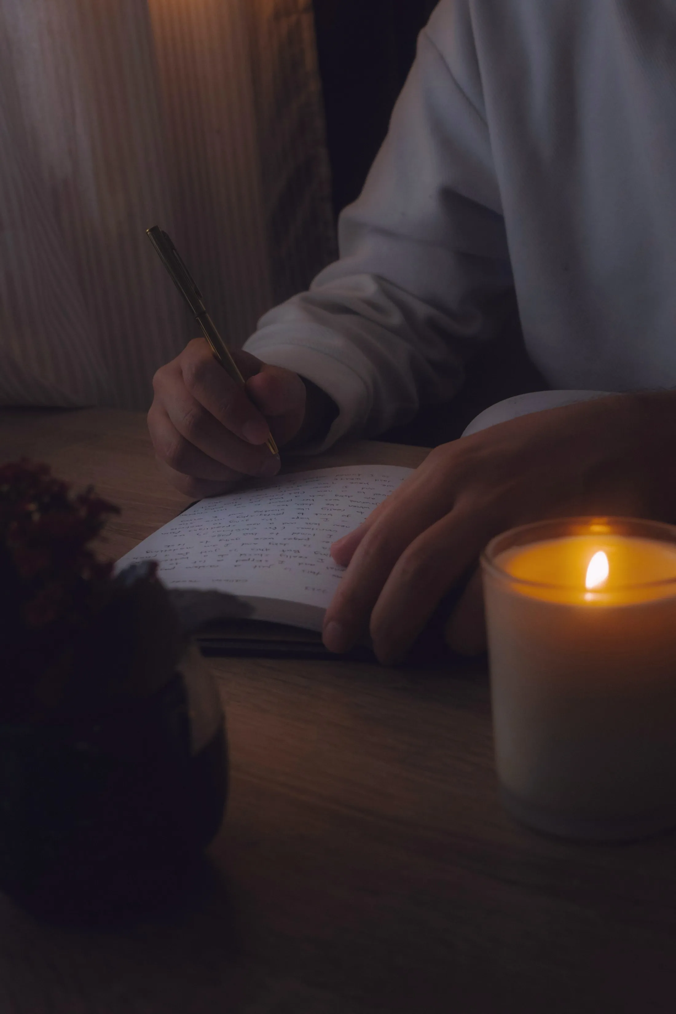 A person writing in a notebook beside a lit candle