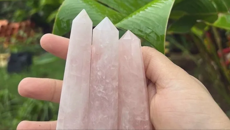 Three pale pink rose quartz towers held in an open hand