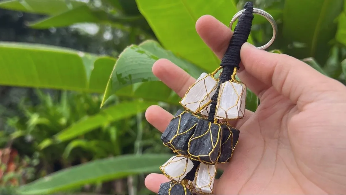 A hanger of white selenite and black tourmaline stones held against green leaves